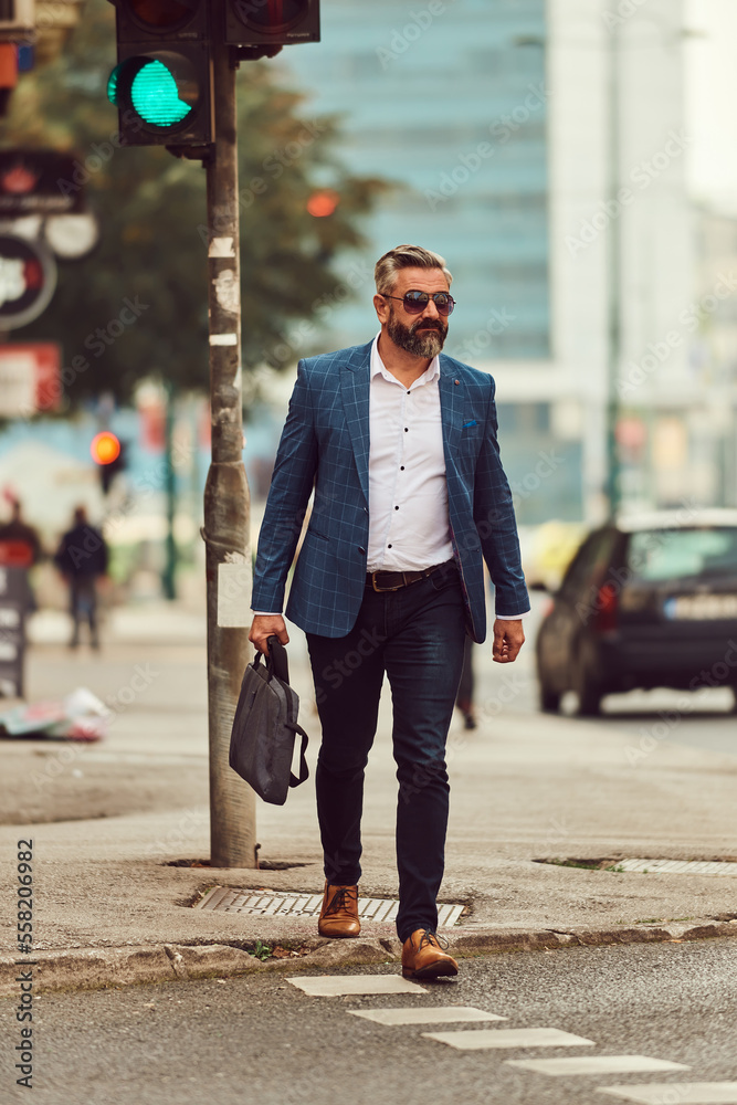 A senior businessman in a blue suit with a briefcase walking through the city A senior businessman in a blue suit with a briefcase walking through the city