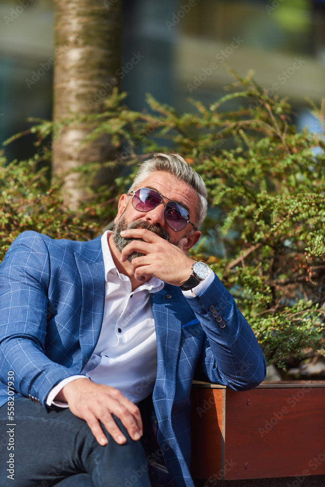 Fototapeta premium Modern senior businessman resting on a bench in the city on a break from work