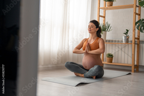 Indoor shot of young fit pregnant woman practicing yoga. Future mother meditating with her eyes closed in the living room. Taking a moment to breathe
