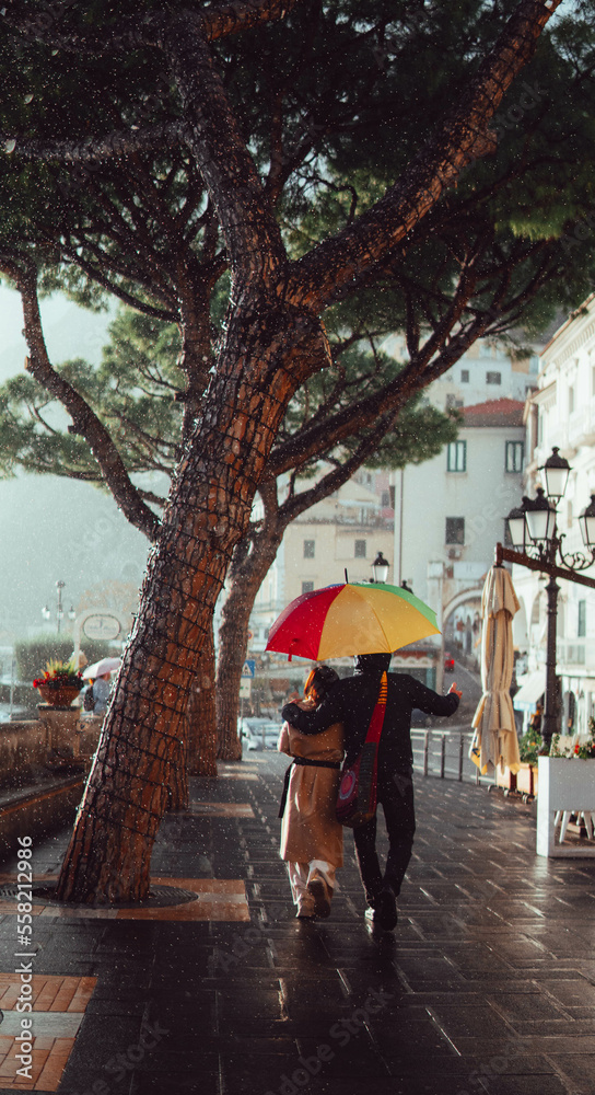 couple under an umbrella strolling along the amalfi coast