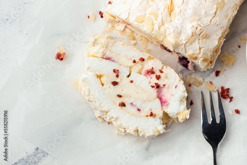 Tableau sur toile Cut of homemade meringue roll decorated with almond flakes and freeze-dried red berries on the white marble background