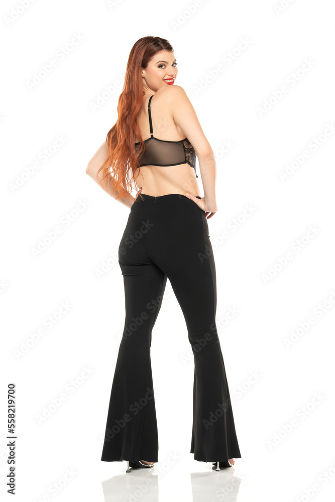 Fashion style studio portrait of beautiful young woman. Black wide leg pants and black lace bra. Model standing and posing against white studio background Fashion style studio portrait of beautiful young woman. Black wide leg pants and black lace bra. Model standing and posing against white studio background