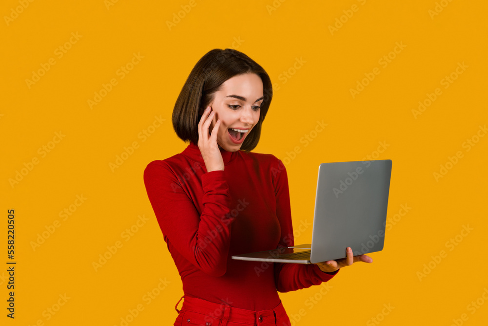 Smiling young lady shopping online, holding laptop on orange Smiling young lady shopping online, holding laptop on orange