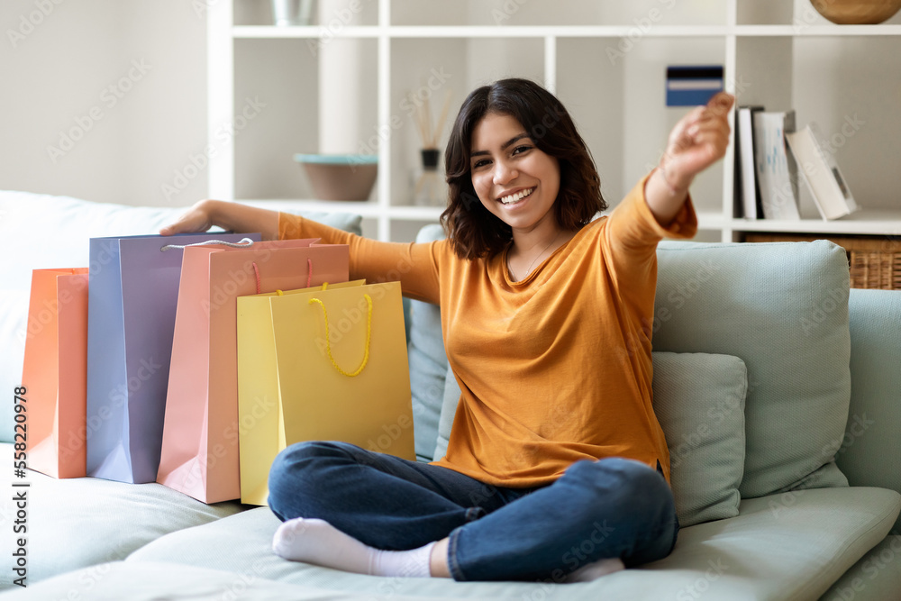 Arab Woman Sitting On Couch With Shopping Bags And Showing Credit Card Arab Woman Sitting On Couch With Shopping Bags And Showing Credit Card