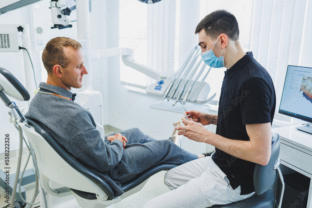 A dentist in a modern dental office tells a patient about dental care. A man sits in a dental chair and listens to a dentist. A dentist in a modern dental office tells a patient about dental care. A man sits in a dental chair and listens to a dentist.