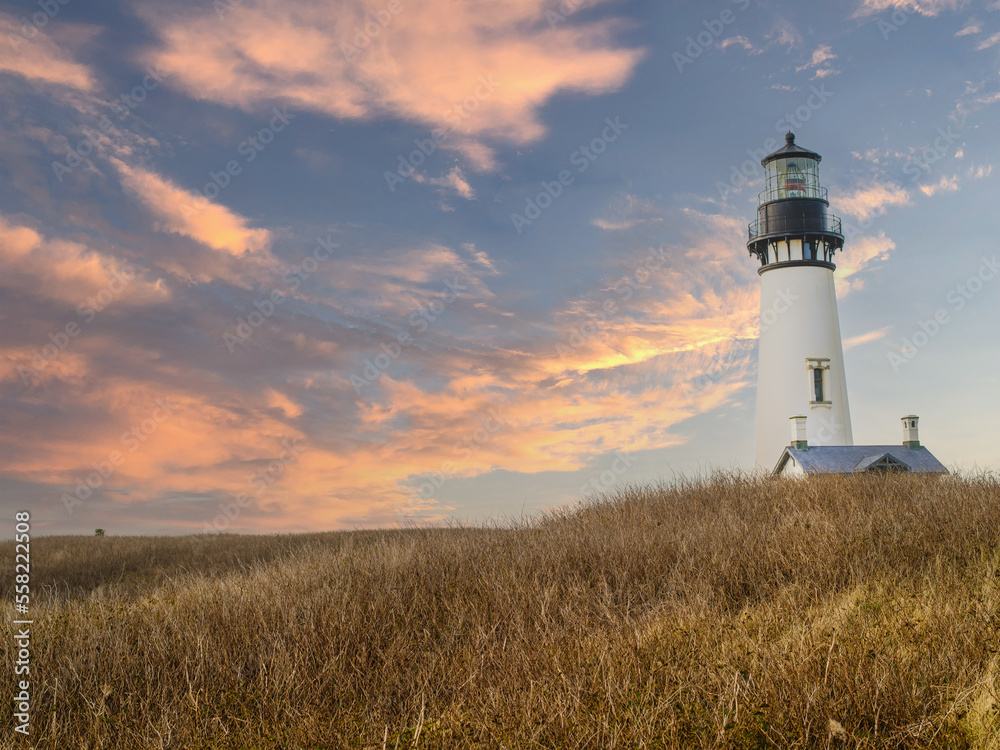 A lighthouse on a high bank under a sky with pink storm clouds. Hilly area with brown withered grass. Beautiful landscape. Tourism, travel, romance, history.