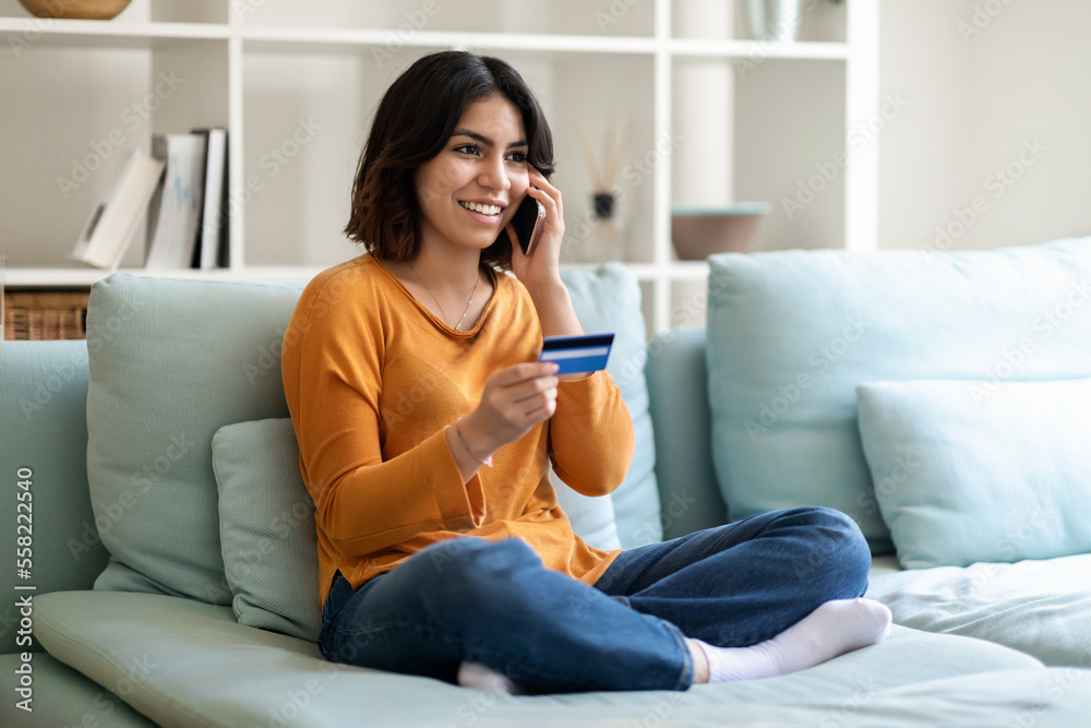 E-commerce Concept. Happy Arab Woman Holding Credit Card And Talking On Cellphone E-commerce Concept. Happy Arab Woman Holding Credit Card And Talking On Cellphone