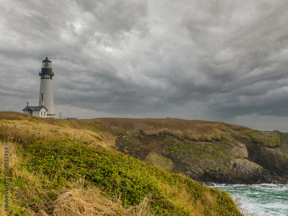 lonely lighthouse on a hilly ocean shore. Rocky shore overgrown with grass, gray storm clouds in the sky. History, tourism, recreation, excursions, architecture.