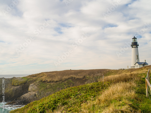 A high bank overgrown with grass and a lighthouse on the shore. Blue sky with white fluffy clouds. Rest  solitude  romance  tourism.