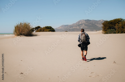 A male photographer with a backpack walks along Patara beach. Panorama of sand dunes.