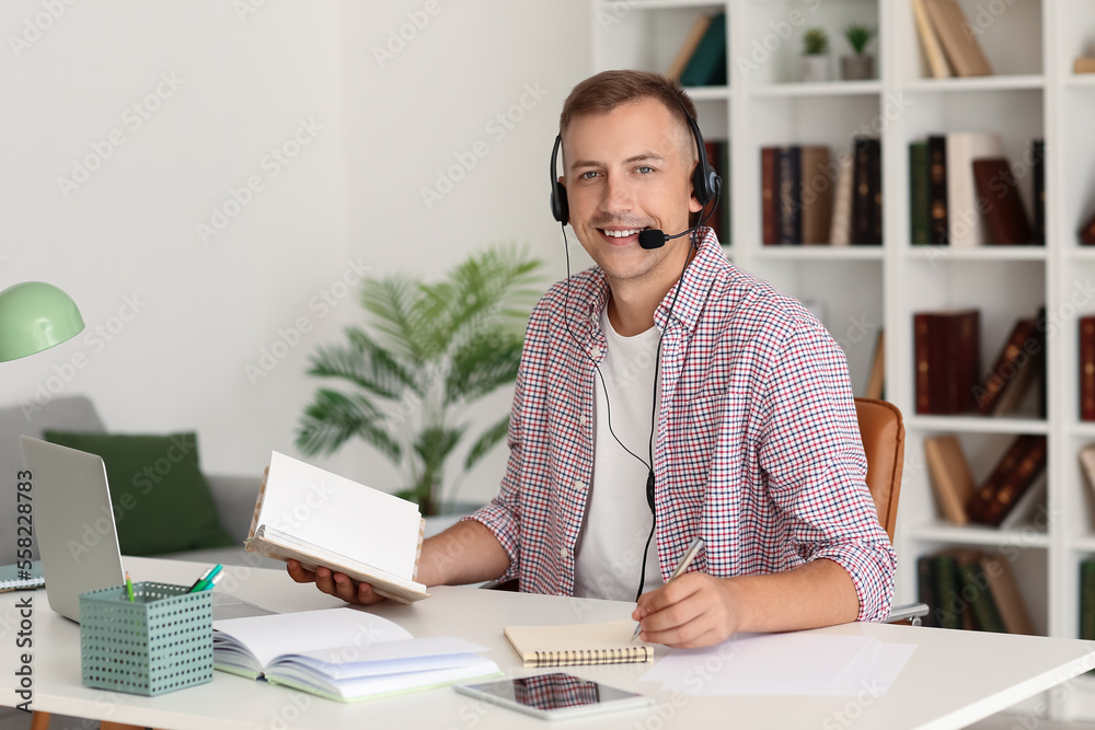Young man with headset and notebook studying online at home