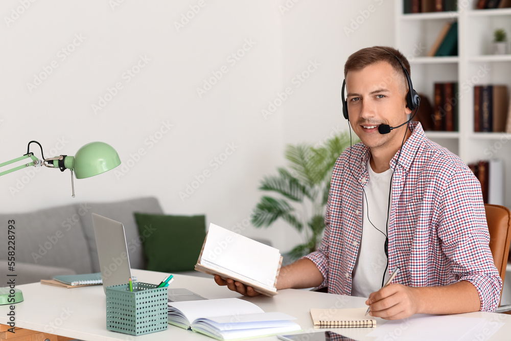 Fototapeta premium Young man with headset and notebook studying online at home