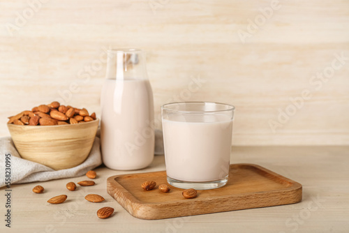 Board with glass of healthy almond milk and nuts on wooden background