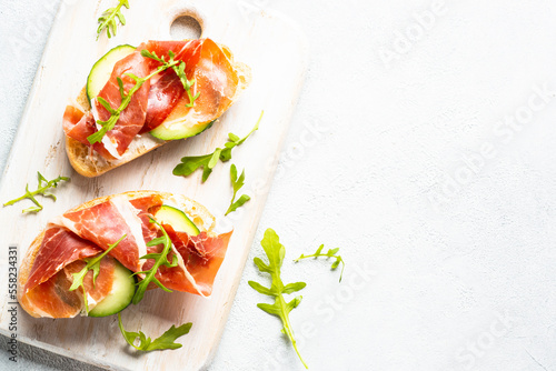 Open sandwiches with cream cheese, prosciutto and arugula at white background. Top view with copy space.
