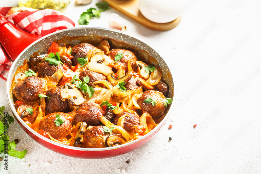 Meatballs with champignon and vegetables stewed in tomato sauce in a frying pan. Top view with copy space at light stone table. Meatballs with champignon and vegetables stewed in tomato sauce in a frying pan. Top view with copy space at light stone table.