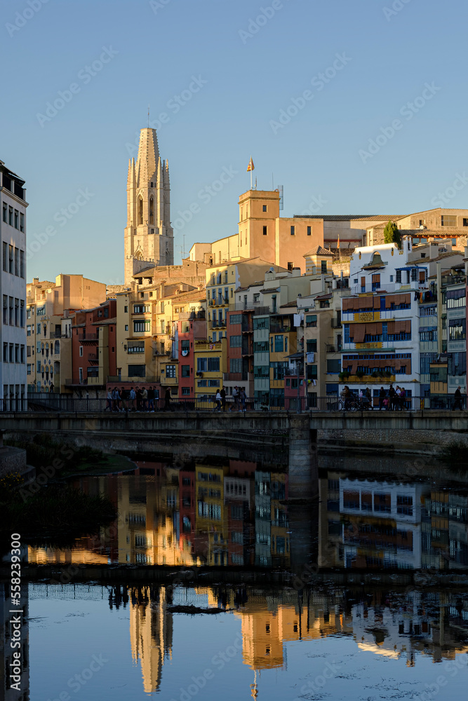 Famous gothic Cathedral landmark over the skyline in Girona reflected with the quiet river houses on a bright sunset blue sky