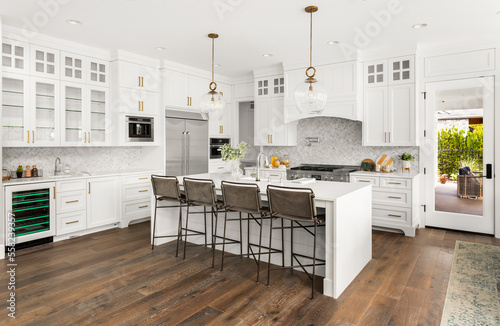 Beautiful white kitchen in new luxury home, with waterfall island, stainless steel appliances, and hardwood floors