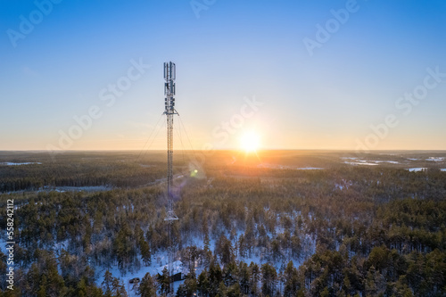 A telecommunications antenna at sunset in a beautiful winter forest landscape. 5G internet mast. Aerial view.