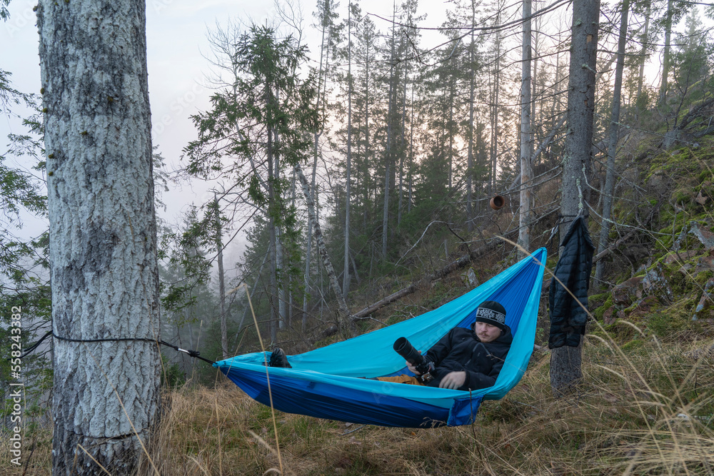 Fototapeta premium Young caucasian male lying and resting in a hammock with camera.