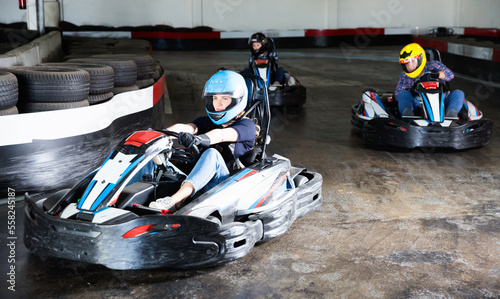 Group of glad cheerful positive people driving go-carts at racing track
