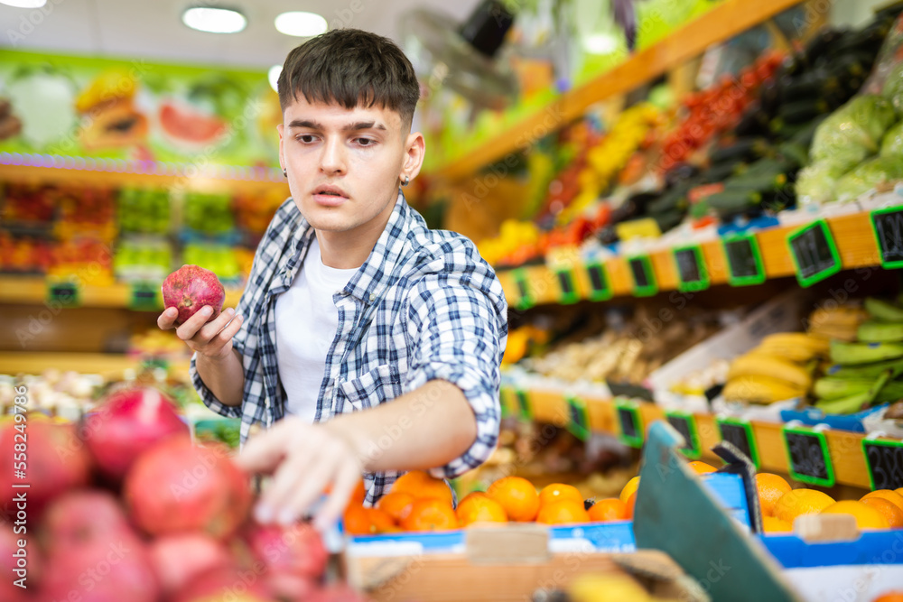 Young man chooses pomegranate fruit on counter of the grocery store