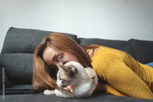 woman in yellow jacket playing with white cat on couch © YerayS