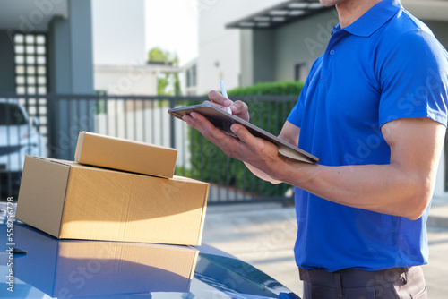 Young deliveryman in blue uniform checking shipping address and information to deliver a package on digital tablet.