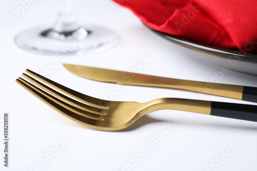 Golden cutlery near plate on white table  closeup