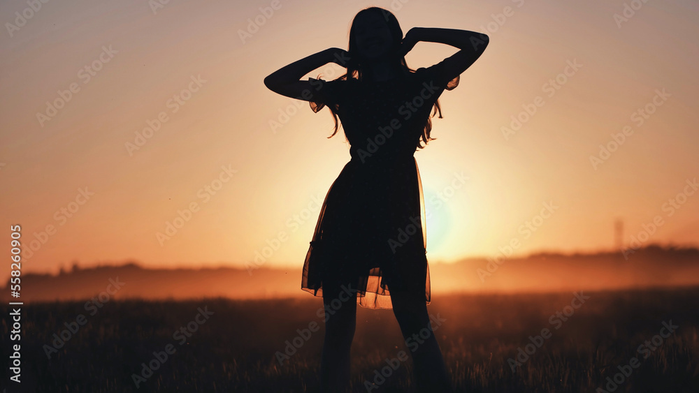 A silhouette of a young girl dancing and spinning on a warm summer evening at sunset.