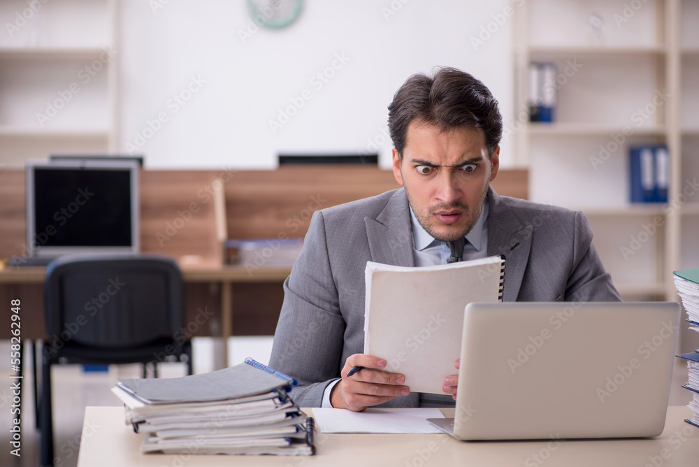 Young male employee unhappy with excessive work in the office Young male employee unhappy with excessive work in the office