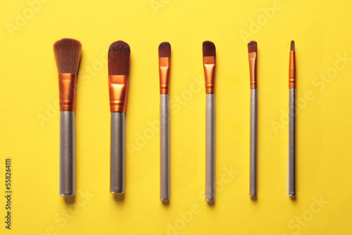 Different makeup brushes on yellow background, flat lay