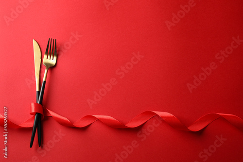 Cutlery set and ribbon on red background  flat lay with space for text. Romantic table setting