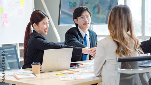 Millennial Asian young professional successful male female businessmen businesswomen in formal suit sitting smiling discussing holding hands showing unity together in company office working desk