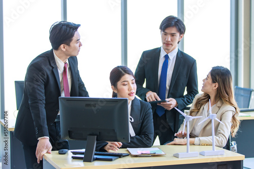 Millennial Asian young professional successful businesswoman in formal suit with female and male businessman colleague in formal suit brainstorming in company office room.