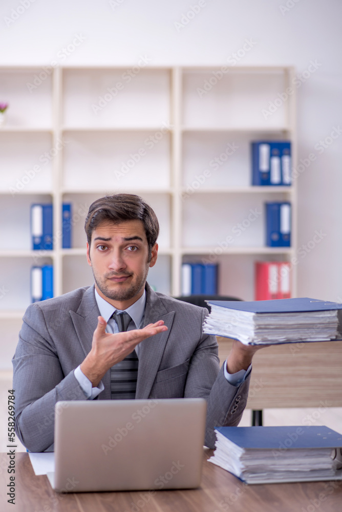 Young male employee unhappy with excessive work in the office Young male employee unhappy with excessive work in the office