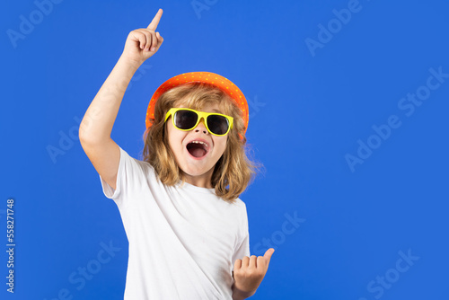Fashion portrait of kid in summer hat, t-shirt and sunglasses on blue studio isolated background. Funny summer fashion kid.