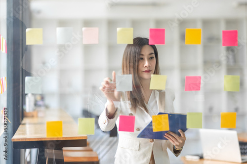 Business female employee with many conflicting priorities arranging sticky notes commenting and brainstorming on work priorities colleague in a modern office. 