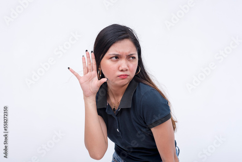 A meddling young woman listening in to the rumor mill. Bending to the left, hands on her ear hearing baseless gossip. Isolated on a white background.