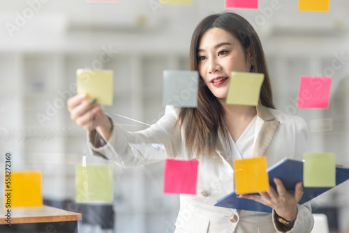 Business female employee with many conflicting priorities arranging sticky notes commenting and brainstorming on work priorities colleague in a modern office.
