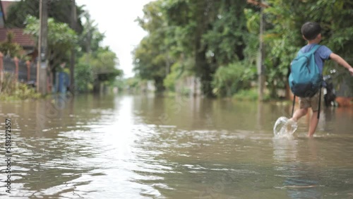 Asian boy struggles to walk across floodwater road with feet wearing sandals.