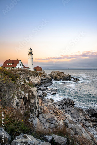 Landscape with a wave-washed operating lighthouse on a rocky shore of the Atlantic Ocean in the rays of the setting sun in the state of Maine in New England