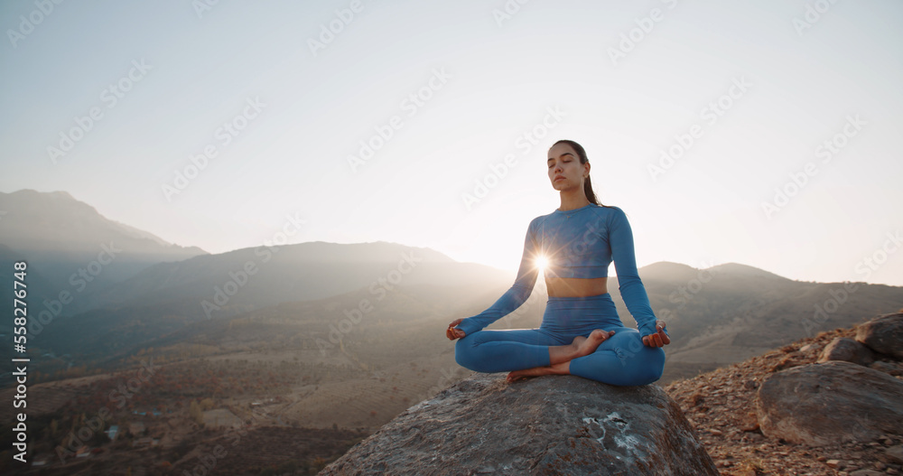 Fit girl doing lotus pose. Young athletic woman meditating in mountains, training and relaxing during sunrise - active lifestyle, zen concept 