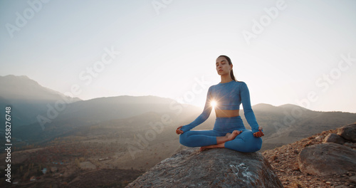 Fit girl doing lotus pose. Young athletic woman meditating in mountains, training and relaxing during sunrise - active lifestyle, zen concept 