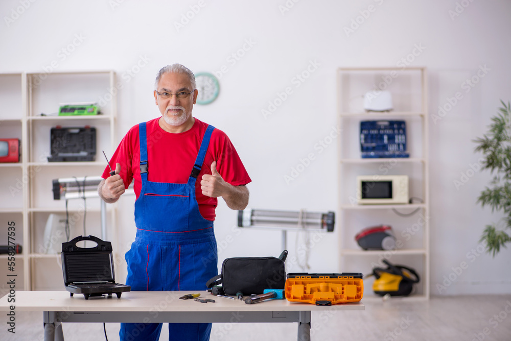 Old repairman repairing sandwich maker at workshop Old repairman repairing sandwich maker at workshop