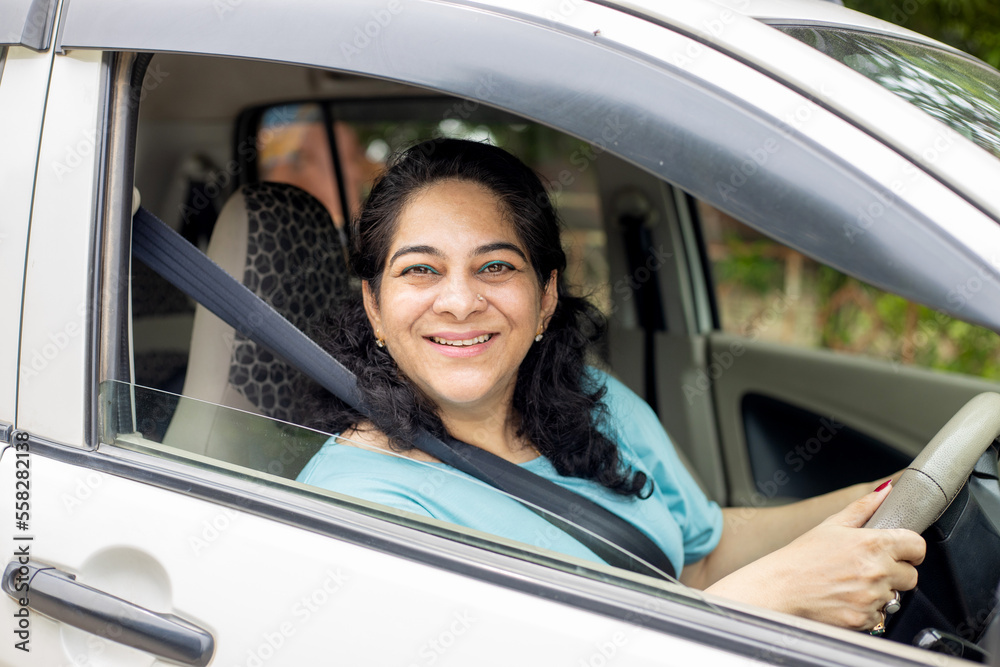 Happy indian mature woman driving a car in city. Safety and people concept.