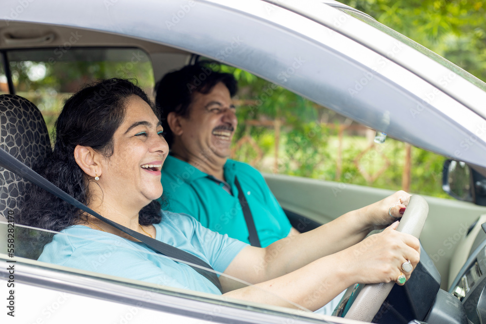 Happy mature indian woman driving car in the city along with her husband. Travel and adventure. People and Safety Concept. Happy mature indian woman driving car in the city along with her husband. Travel and adventure. People and Safety Concept.