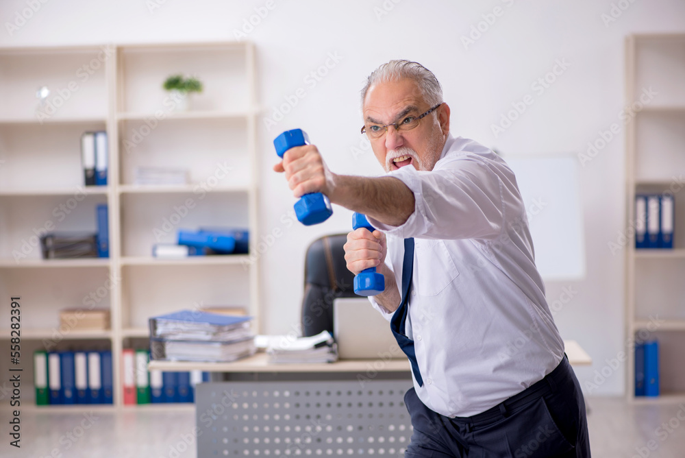 Old male employee doing sport exercises at workplace Old male employee doing sport exercises at workplace