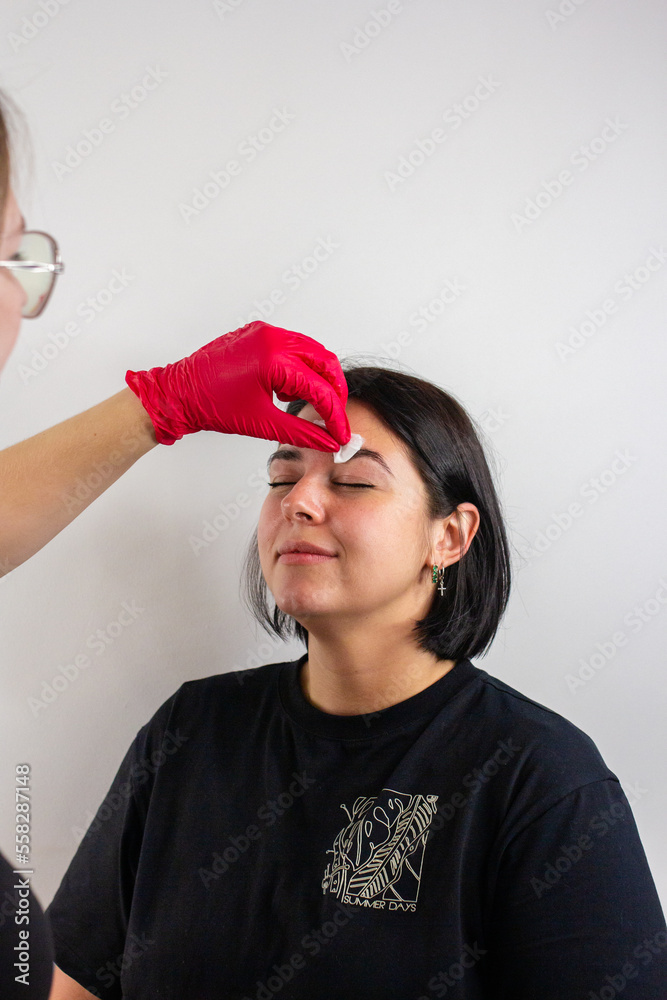 Eyebrow master making correction of eye brows of client woman in beauty salon