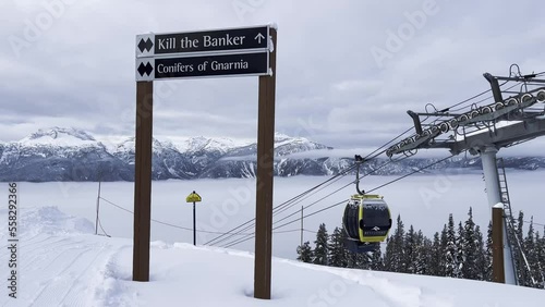 Double black diamond ski run sign on the top of Revelstoke Mt MacKenzie ski Resort with moving gondalas in the background and a view of the snowy mountains. photo