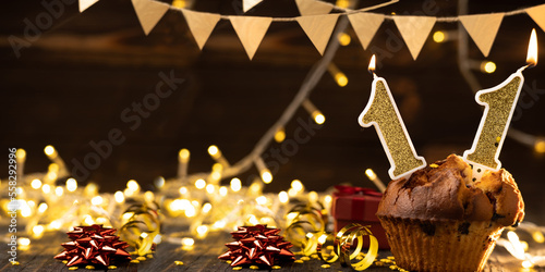 Number 11 gold burning candle in a cupcake against celebration wooden background with lights. Birthday cupcake. Copy space. photo